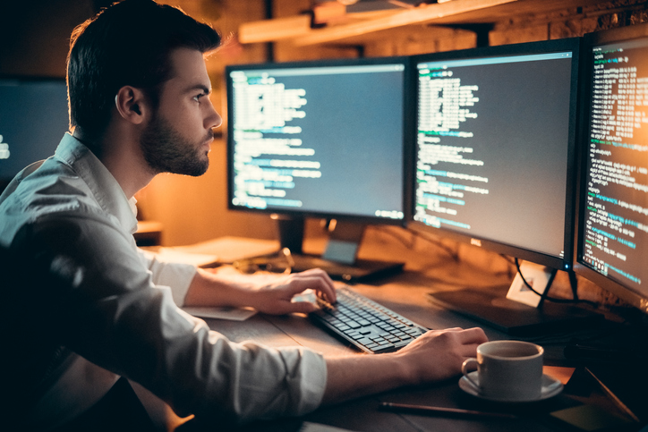 Focused marketer reviewing marketing analytics and ROI on computer monitors working late in office
